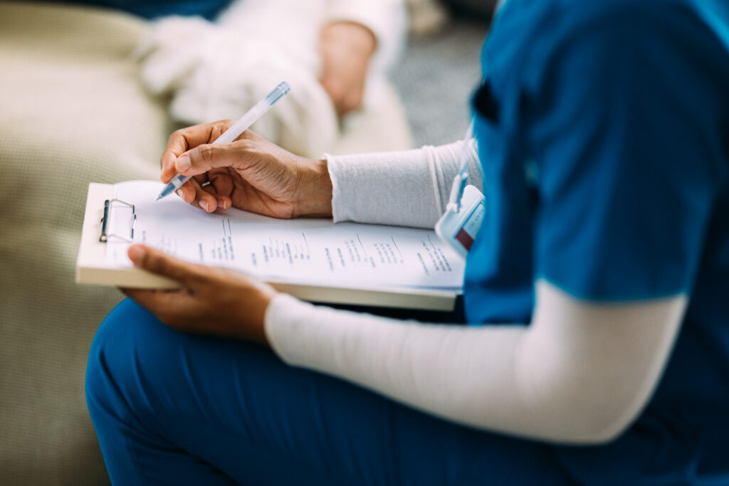A nurse is writing on a clipboard during a patient consultation, representing healthcare communication, professionalism, and patient care.
